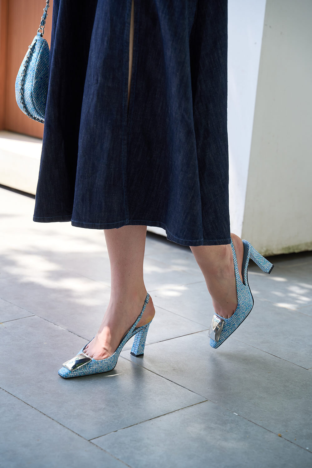 Person wearing a dark coat and blue high-heeled shoes on a pavement.